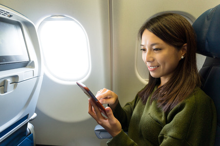 Woman using mobile phone inside airplaneの写真素材