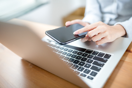 Woman hand touch phone over laptop keyboardの写真素材