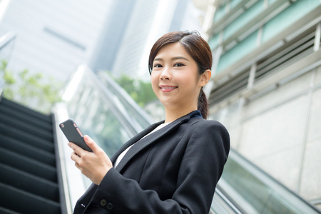 Young businesswoman hold with mobile phone and standing at escalatorの写真素材