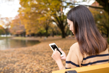 Asian woman using mobile phone at autumn seasonの写真素材