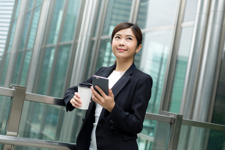 Businesswoman holding coffee cup and cellphoneの写真素材