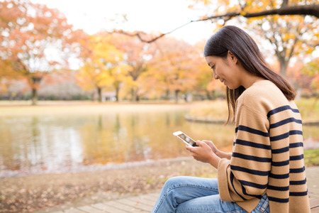 Woman using cellphone at autumn fall tree parkの写真素材