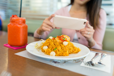 Woman taking photo on fried noodles with cellphoneの写真素材