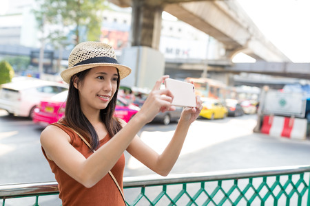 Woman taking photo on mobile phone in Bangkokの写真素材