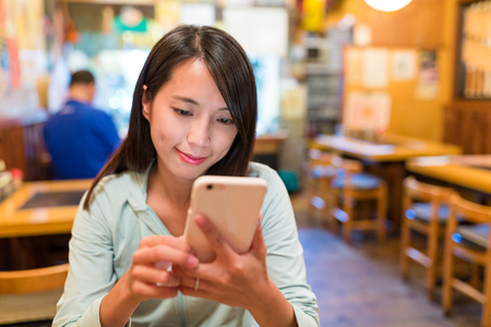 Woman looking at mobile phone in japanese restaurantの写真素材