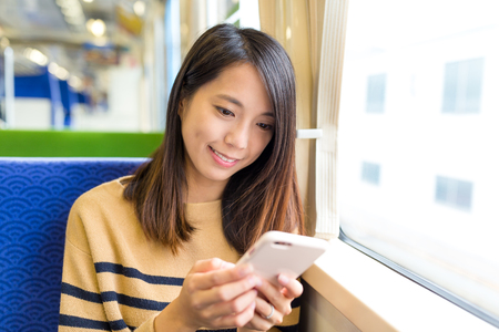 Woman sending sms on mobile phone in trainの写真素材