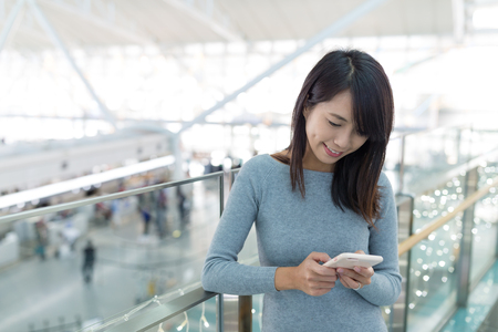Woman working on mobile phone in airportの写真素材