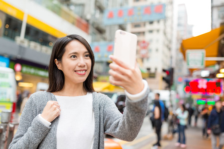 Woman taking selfie by mobile phone at street of Hong Kongの写真素材