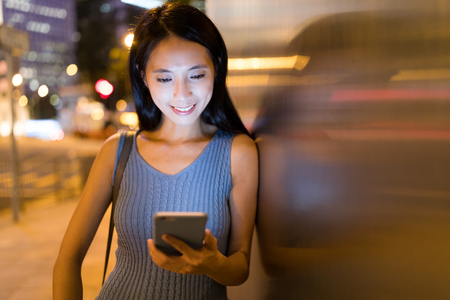 Woman using cellphone in the city at nightの写真素材