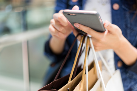 Close up of woman using cellphone and holding shopping bags の写真素材