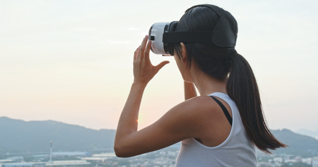 Woman playing game on VR device in sunset time の写真素材