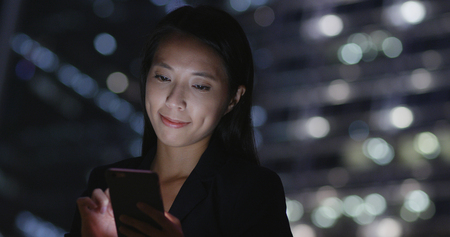 Businesswoman working on cellphone at nightの写真素材