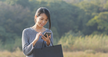 Woman holding cellphone and paper bag の写真素材