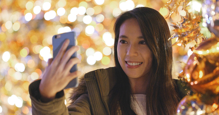 Woman taking selfie on mobile phone over christmas tree decoration の写真素材