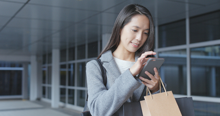 Woman using cellphone and holding paper bag の写真素材