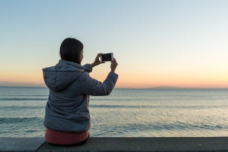 Woman taking photon with seascape and sunsetの写真素材