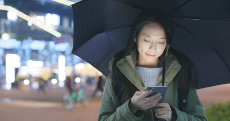 Woman look at mobile phone and bringing an umbrella の写真素材