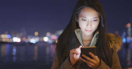 Woman using cellphone in city at night の写真素材