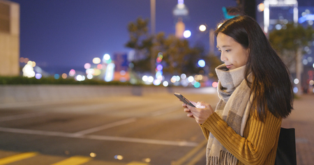 Woman waiting for walking in the traffic road and look at the cellphone の写真素材