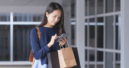 Woman use of mobile phone and holding shopping bag の写真素材