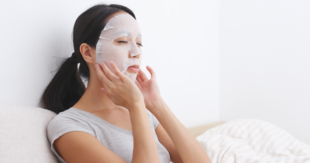 Woman having facial mask on bed の写真素材