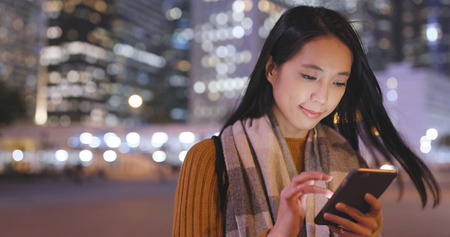 Woman use of smart phone and standing beside traffic street at night の写真素材