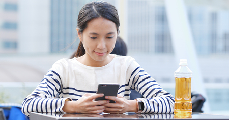Woman look at mobile phone and drink of bottle of tea の写真素材