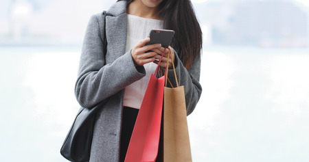 Woman use of smart phone and holding with shopping bag の写真素材