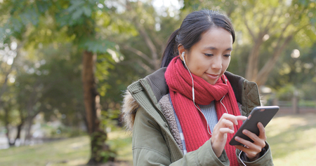 Woman enjoy listening the song on mobile phone with wearing the earphone at chinese gardenの写真素材