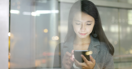 Business woman use of smart phone in city with window reflection at nightの写真素材