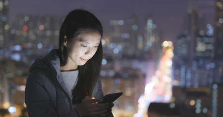 Woman use of mobile phone over city at nightの写真素材