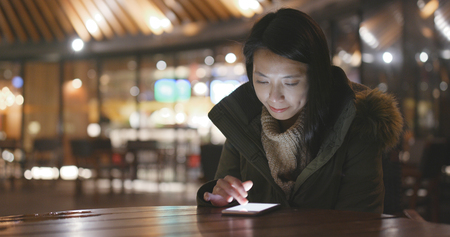 Woman using mobile phone outside restaurant at nightの写真素材