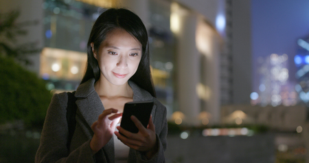 Business woman use of smart phone in city at nightの写真素材
