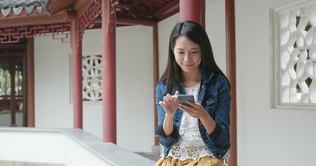 Woman sending sms on cellphone in Chinese gardenの写真素材