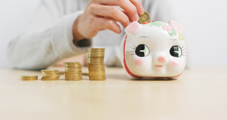 Putting golden coins into piggy bank at homeの写真素材