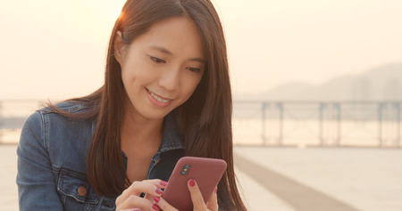 Young woman use of mobile phone with sun flareの写真素材