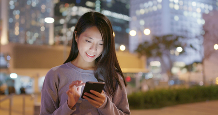 Woman use of smart phone in city at nightの写真素材