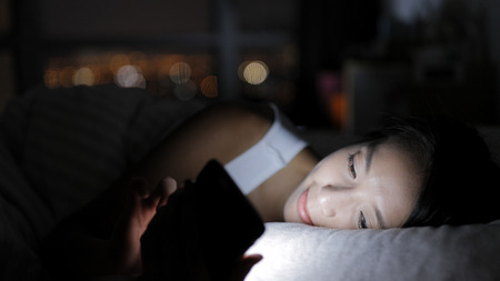 Woman looking at smart phone and lying on bedの写真素材