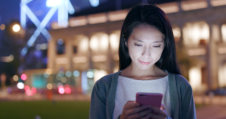 Woman look at smart phone in city at nightの写真素材