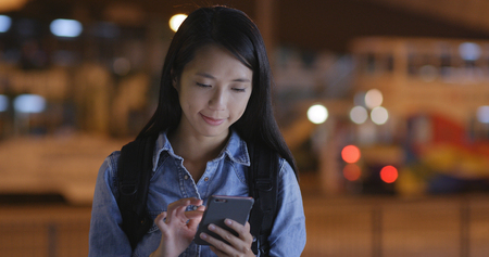 Young woman looking at mobile phone in city at nightの写真素材