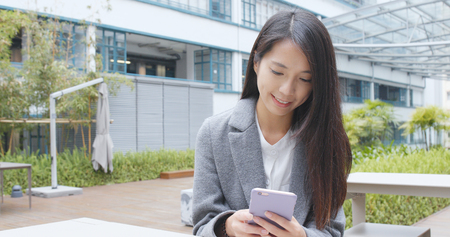 Business woman working on mobile phone in the parkの写真素材
