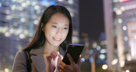 Business woman reading on smart phone in city at nightの写真素材