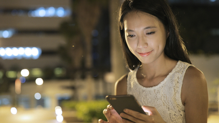 Woman looking at mobile phone at nightの写真素材
