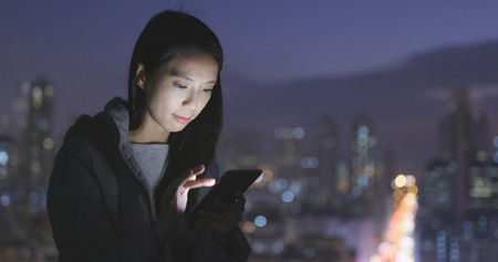 Woman using mobile phone over city at nightの写真素材