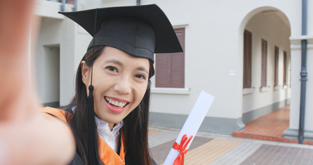 Asian woman wearing graduation gown and taking self imageの写真素材