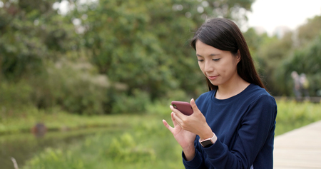 Young woman using smart phone and sitting on wooden bridgeの写真素材