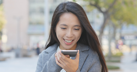 Business woman sending audio message on cellphone at outdoorの写真素材