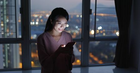 Woman look at mobile phone at night inside living roomの写真素材