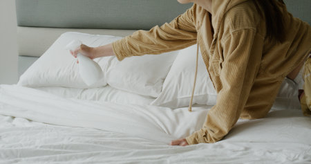 Housewife use disinfection alcohol spray on her bed at homeの写真素材