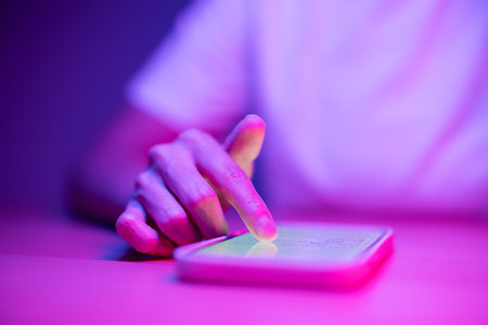 Woman use mobile phone on the table under pink lightの写真素材